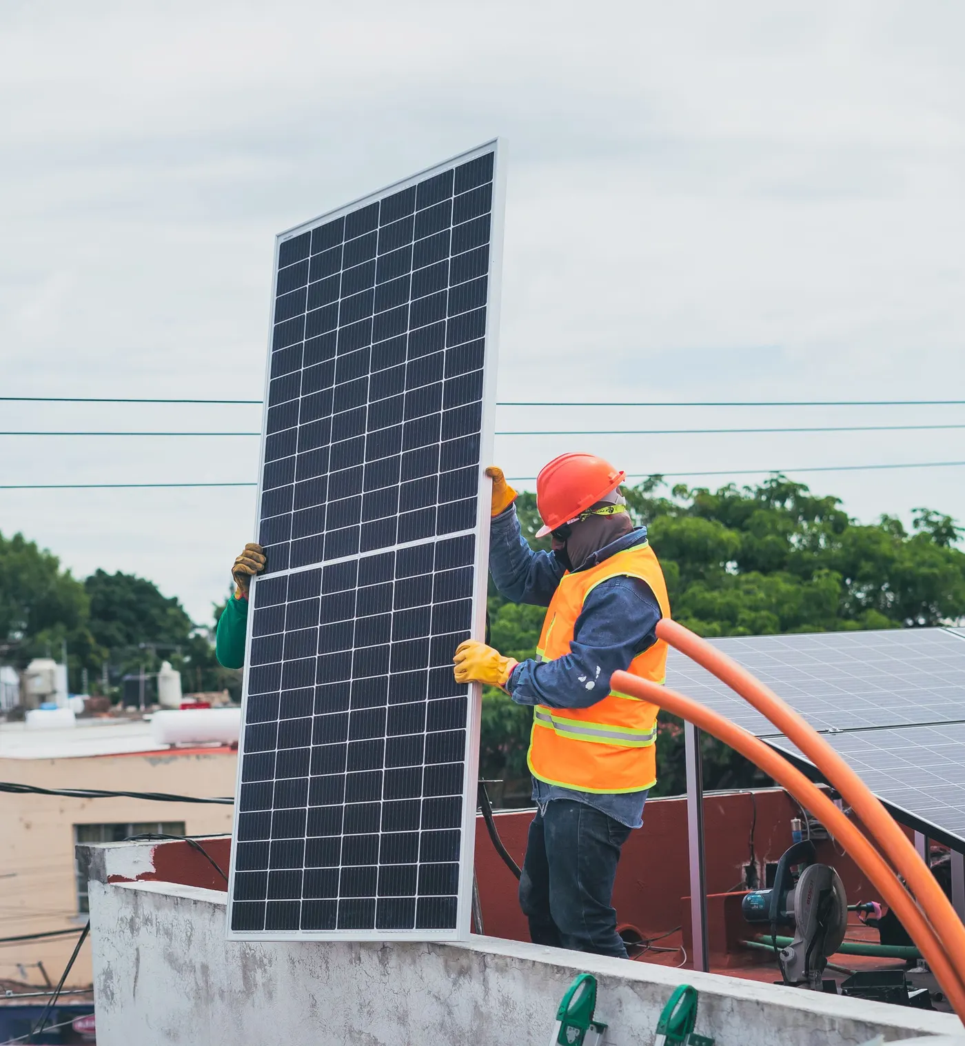 An installer carrying a panel across a city rooftop
